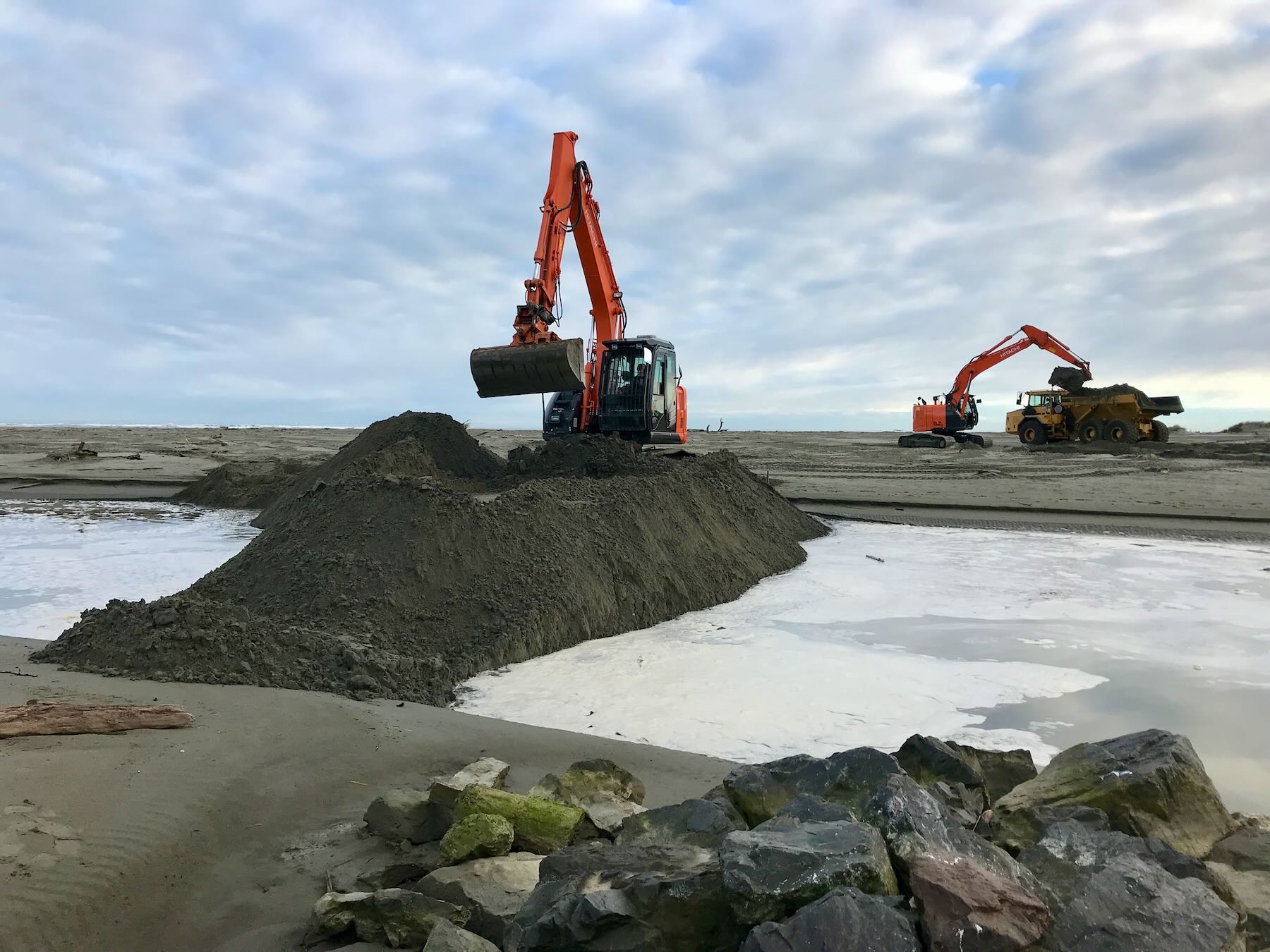 Diggers work with piles of sand on the beach in June 2018. 